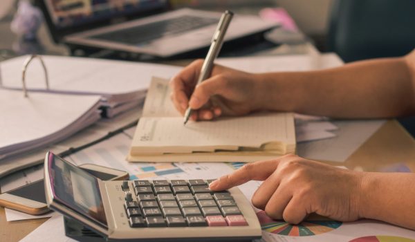 Man hand using a financial calculator with writing make note and Financial data analyzing on desk at home